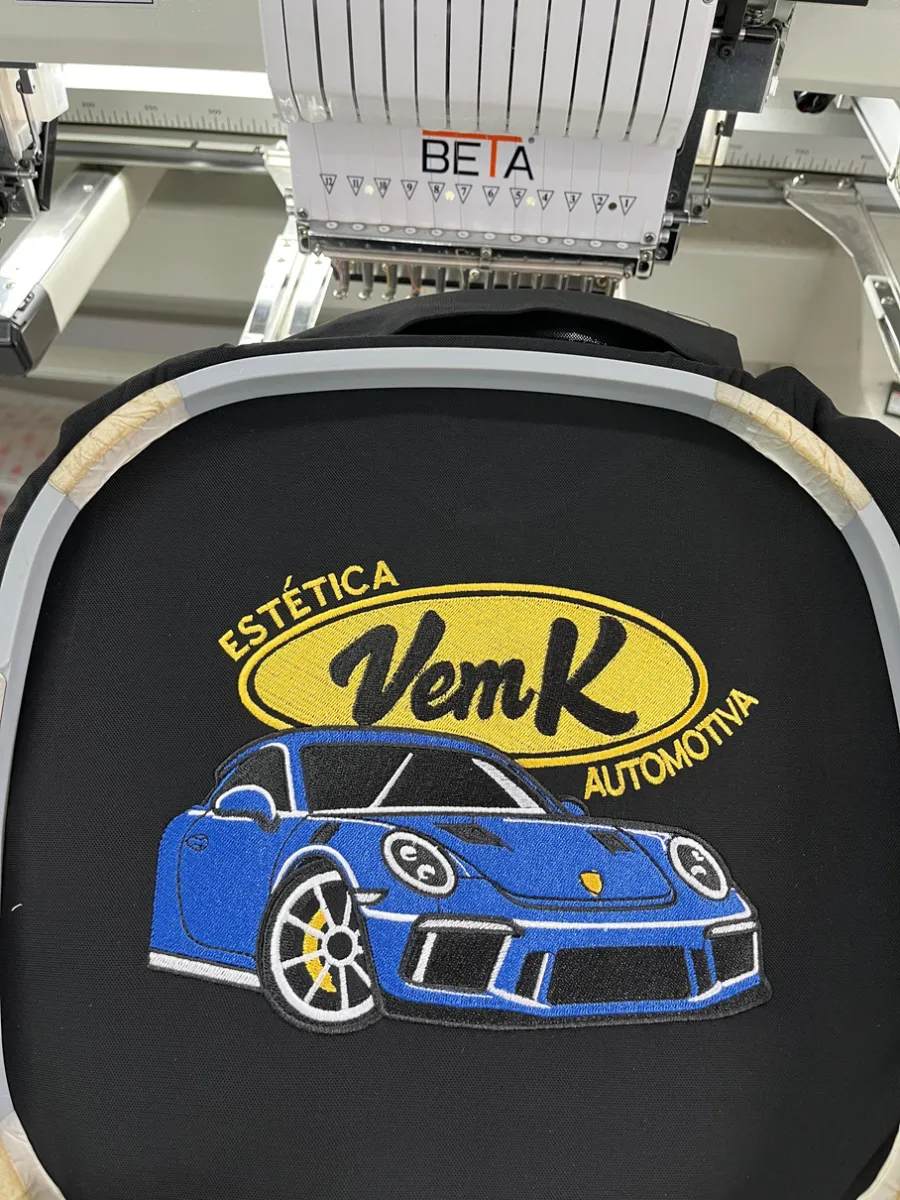 Carro bordado em camisa preta, ainda no bastidor da máquina